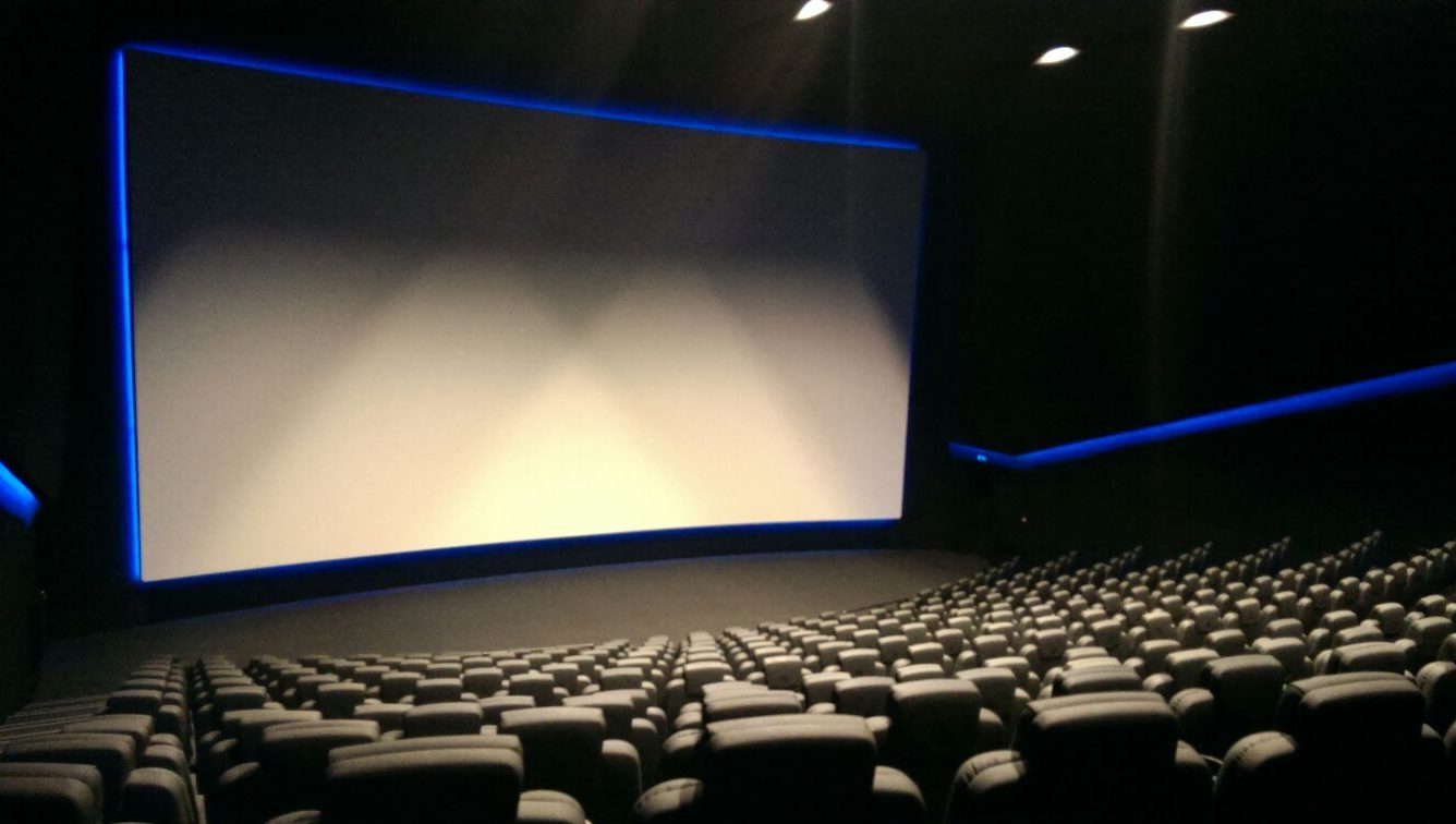 A large empty cinema with black seats facing a large blank screen