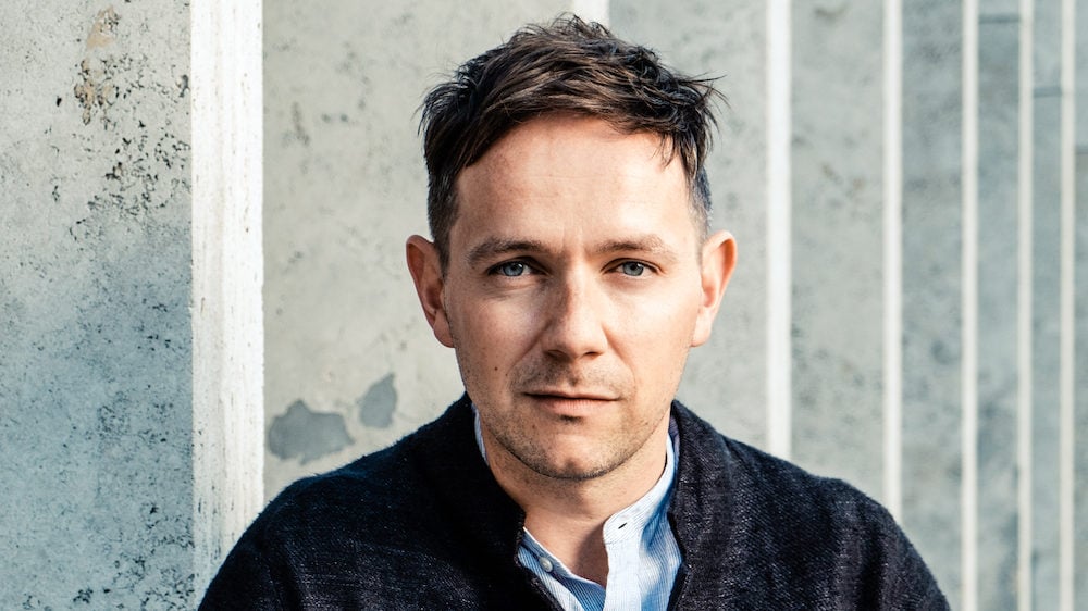 Iestyn Davies sits in front of a grey wall