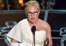 Patricia Arquette stands on stage with an Oscar statuette and a sheet of paper, speaking into a microphone.