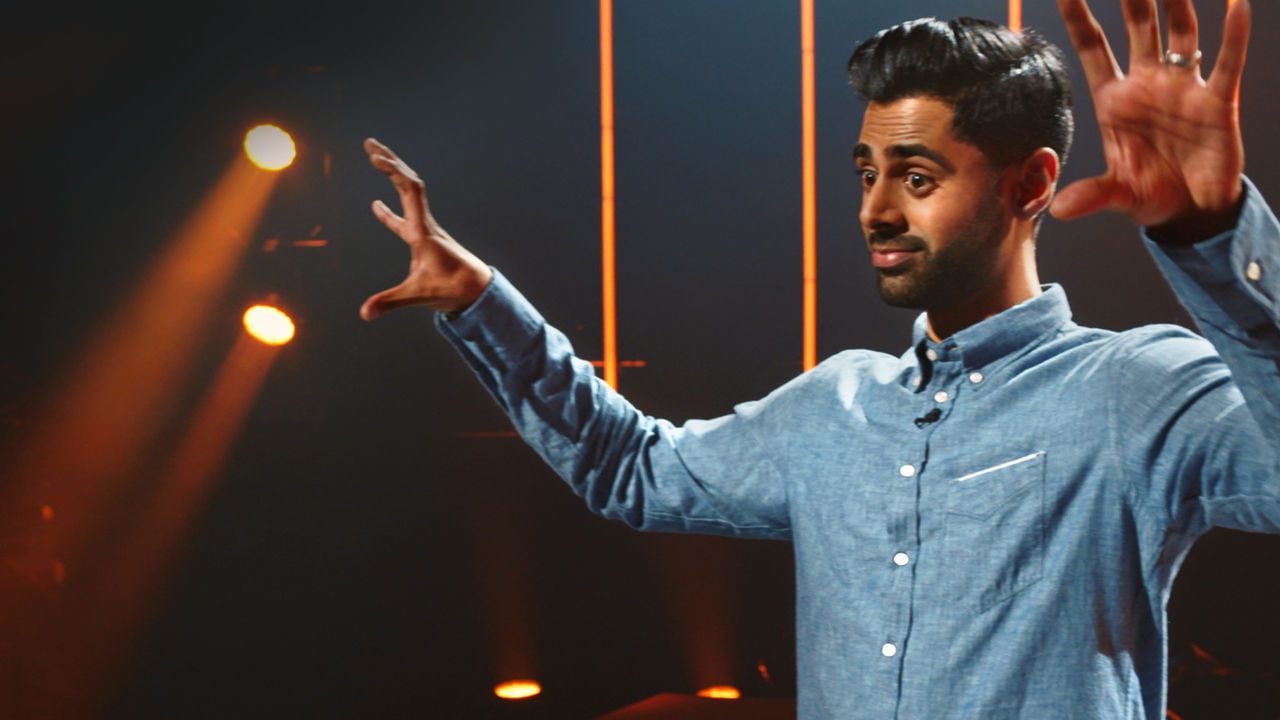 The comedian Hasan Minhaj raises his arms during a comedy set.