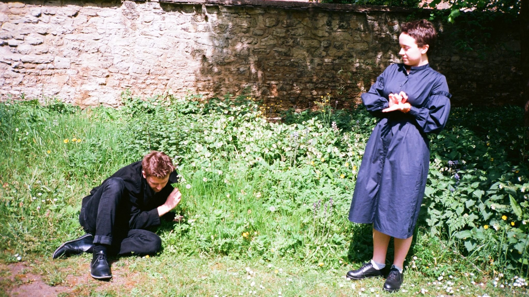 A man huddles on the grass with a woman looking over him