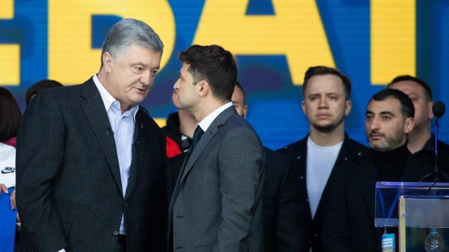 The image shows Petro Poroshenko and Vladimir Zelensky engaging in a debate on the 19th of April 2019. They are in front of a blue background.