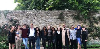 The cast and crew of the play standing in a row in a garden setting with their arms around each other