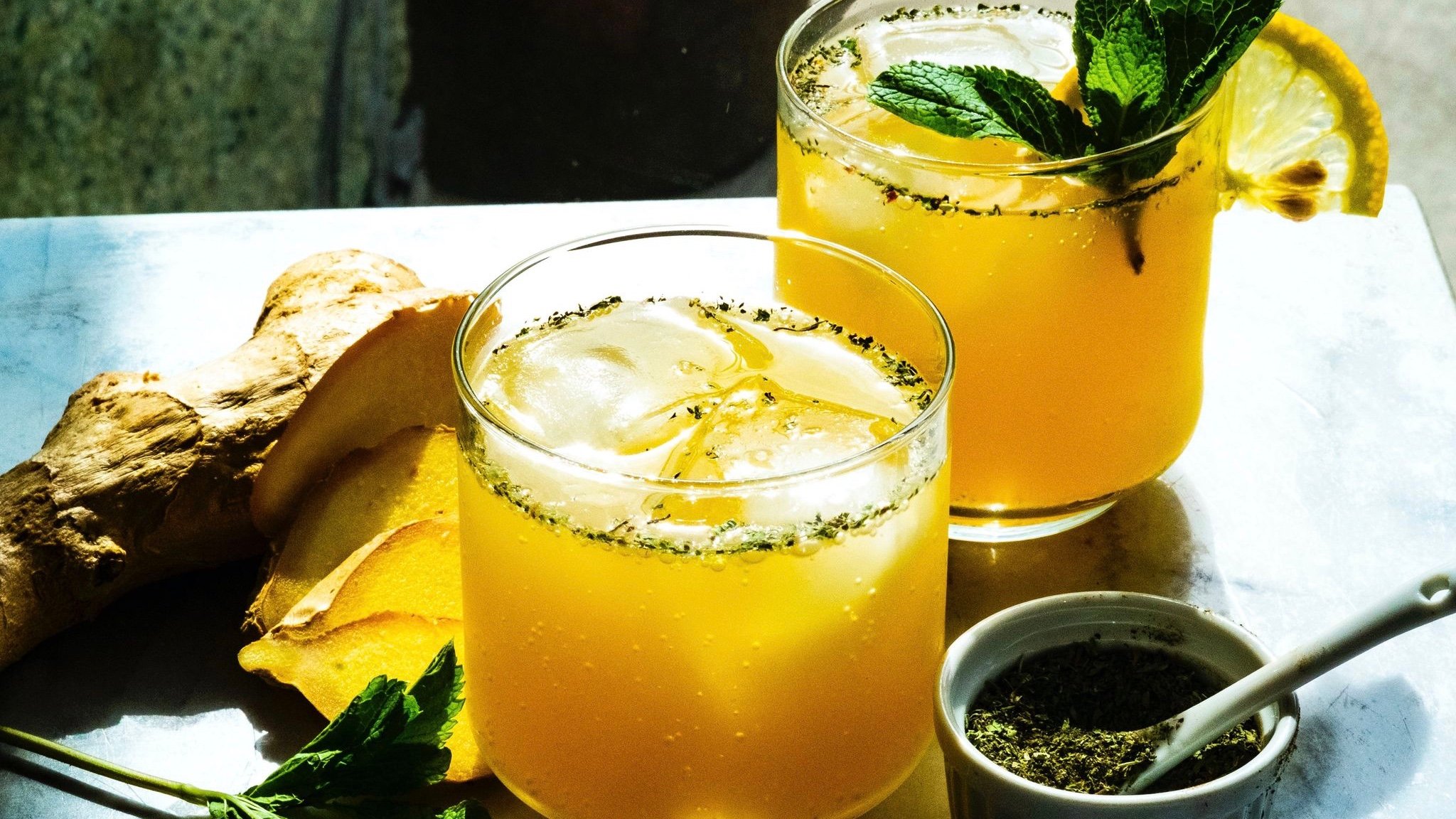 Two orange drinks sit in sunlight, surrounded by ingredients