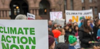A sign saying "CLIMATE ACTION NOW" on the left, with protestors in the background.