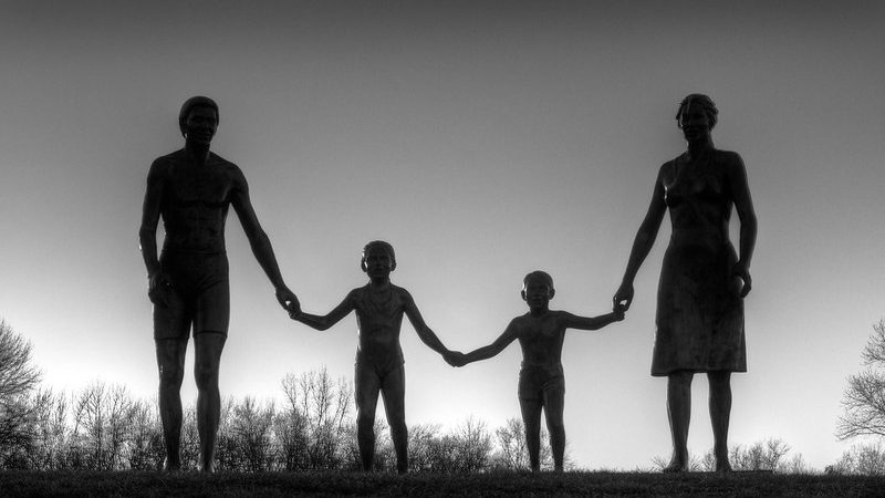 A naturalistic statue of a father, mother and two sons, all holding hands against a grey sky