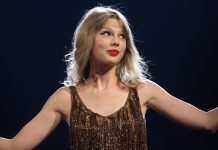 Taylor Swift stands against a black background with her arms outstretched