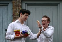 A man in a white shirt holds an armful of snacks and grabs the wrist of another man in a white shirt, who is holding an Edcles cake and looking scared.
