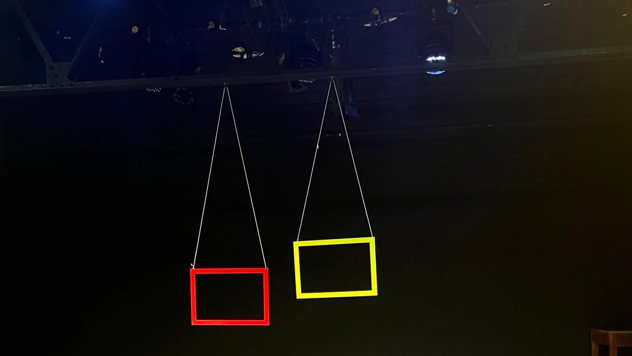 Two yellow and red frames hanging from the ceiling against a dimly-lit background
