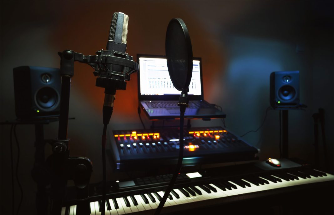 A small recording studio equipped with a keyboard, mixing desk, laptop, microphone, speakers, and intimate lighting