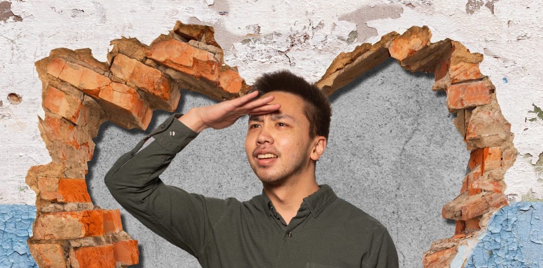 Man looking out from within heart-shaped hole in wall.