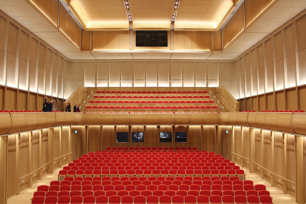 The seats in the Sohmen Concert Hall viewed from the stage. Red cushioned seats line the bottom floor and the seats on the upper floor are tiered